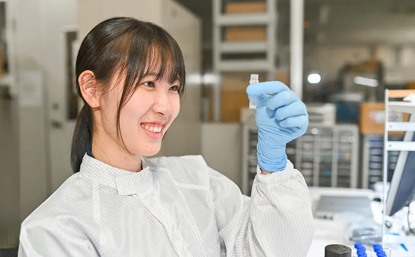 白衣姿の女性研究員が実験室でサンプルを笑顔で確認している様子